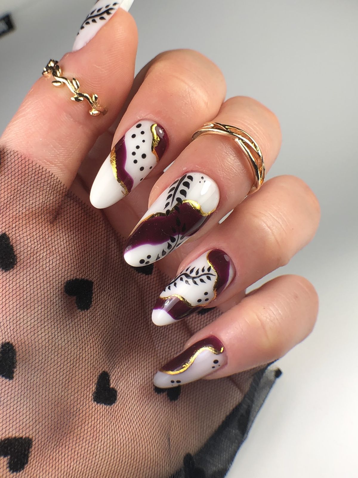 Witte amandelnagels met bordeauxrode en zwarte blaadjes en goud